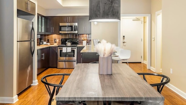 A modern kitchen with stainless steel appliances, a wooden dining table, and a pendant light. - Walkers Paradise & Stunning Eclectic Digs! (Memphis)