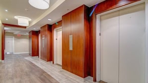 A hotel corridor with wooden paneling, white elevators, and a tiled floor. - Walkers Paradise & Stunning Eclectic Digs! (Memphis)