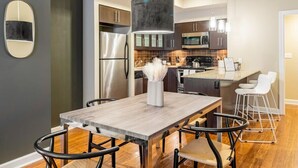 A modern kitchen with a wooden dining table, black chairs, a stainless steel refrigerator, and a large island with bar stools. - Walkers Paradise & Stunning Eclectic Digs! (Memphis)
