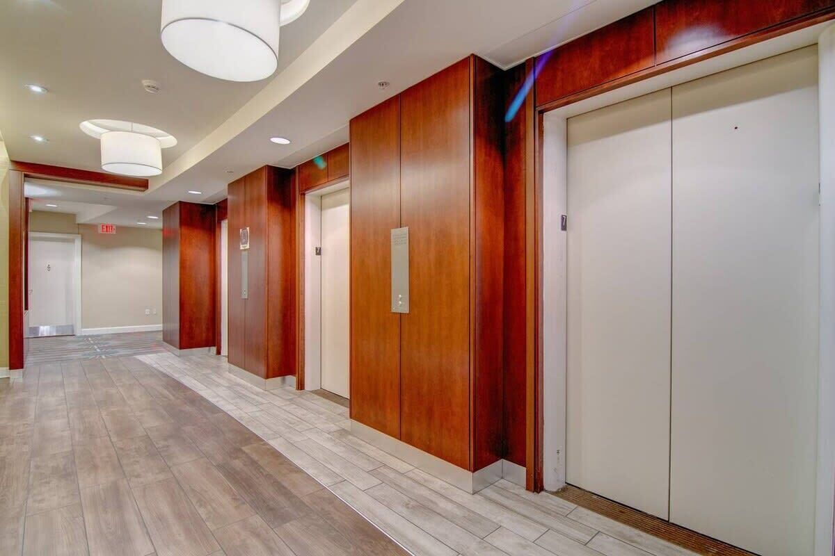A hotel corridor with wooden paneling, white elevators, and a tiled floor.