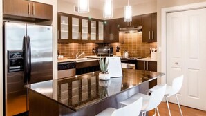 Una cocina moderna con refrigerador de acero inoxidable, gabinetes de madera oscura, una isla con encimera de granito y sillas blancas.
