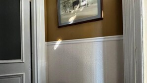 Un couloir avec un banc, un tableau encadré au mur et une porte.