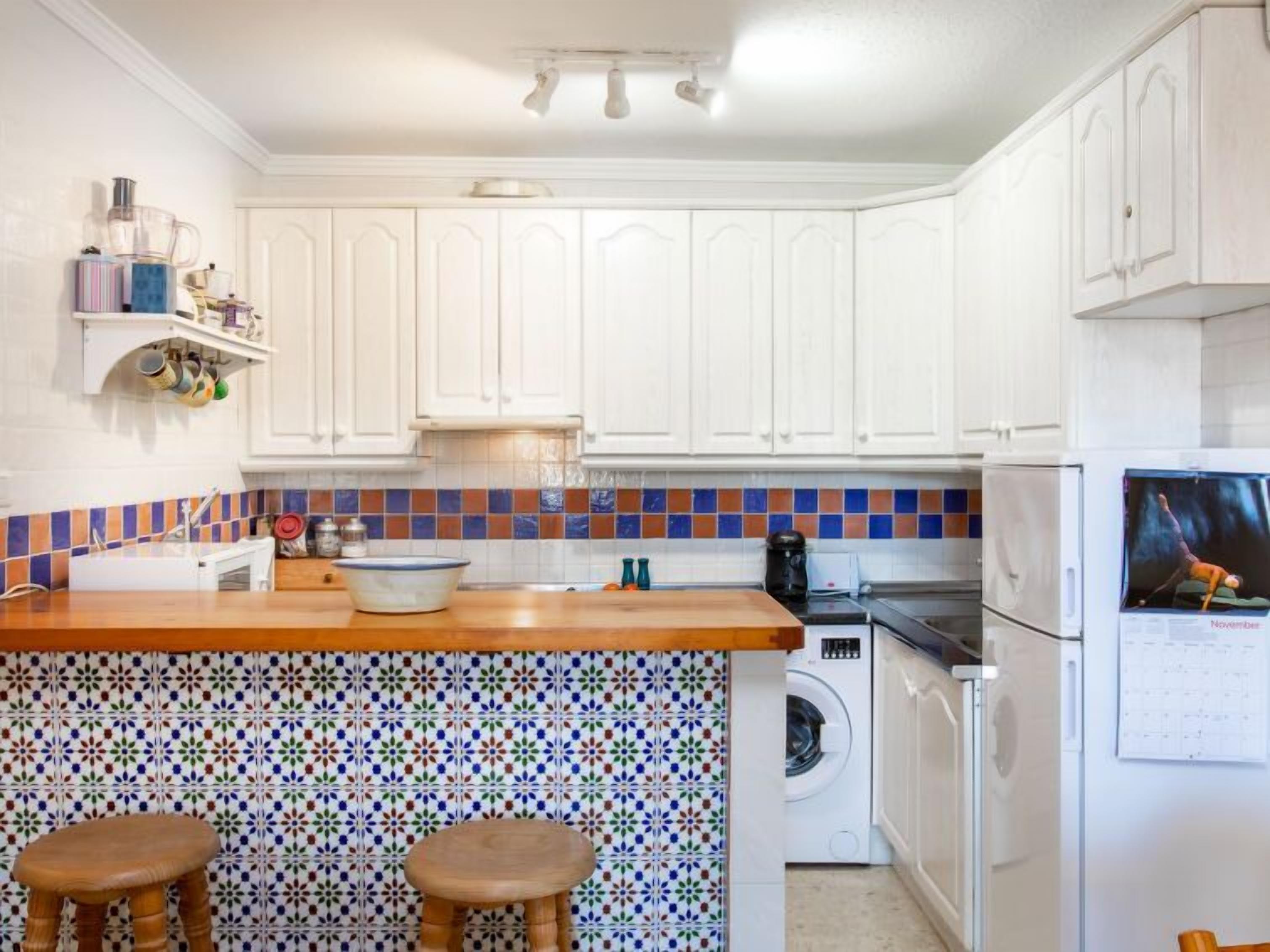 A kitchen with white cabinets, a tiled backsplash, a wooden countertop, a washing machine, and a refrigerator.