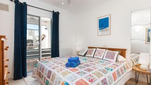 A bedroom with a large bed, a ceiling fan, a view of the outside balcony, and a framed picture on the wall.