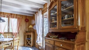 Un intérieur en bois comprenant un coin repas, un meuble avec des portes en verre et une fenêtre avec des rideaux.