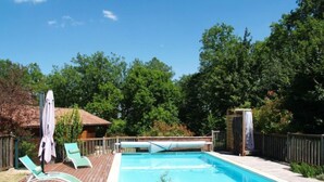Une piscine rectangulaire dotée d’une terrasse en bois, entourée d’une clôture en bois et d’arbres.