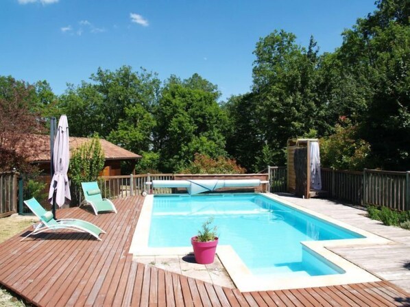 A rectangular swimming pool with a wooden deck, surrounded by a wooden fence and trees.