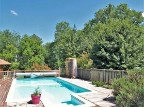 A rectangular swimming pool with a wooden deck surrounding it, set in a lush, green forested area.