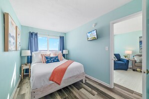 A bedroom with a bed, a window, a door leading to another room, and a view of the outside.