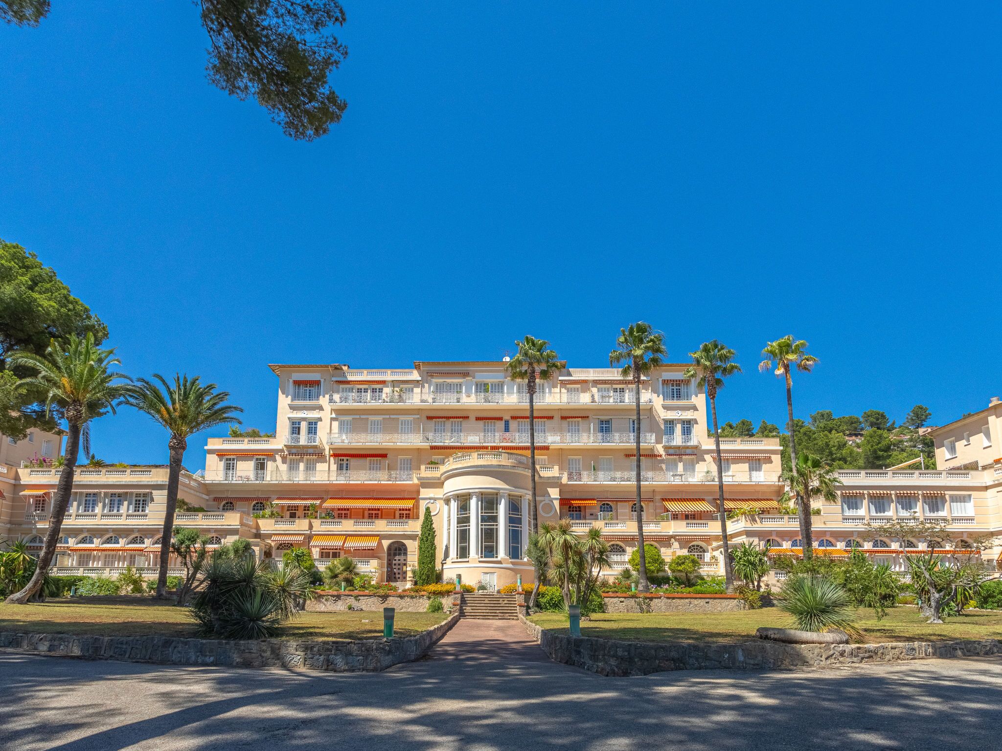A multi-story hotel with a central courtyard, palm trees, and a clear blue sky.
