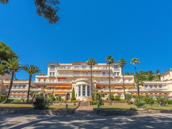 A multi-story hotel with a central courtyard, palm trees, and a clear blue sky.