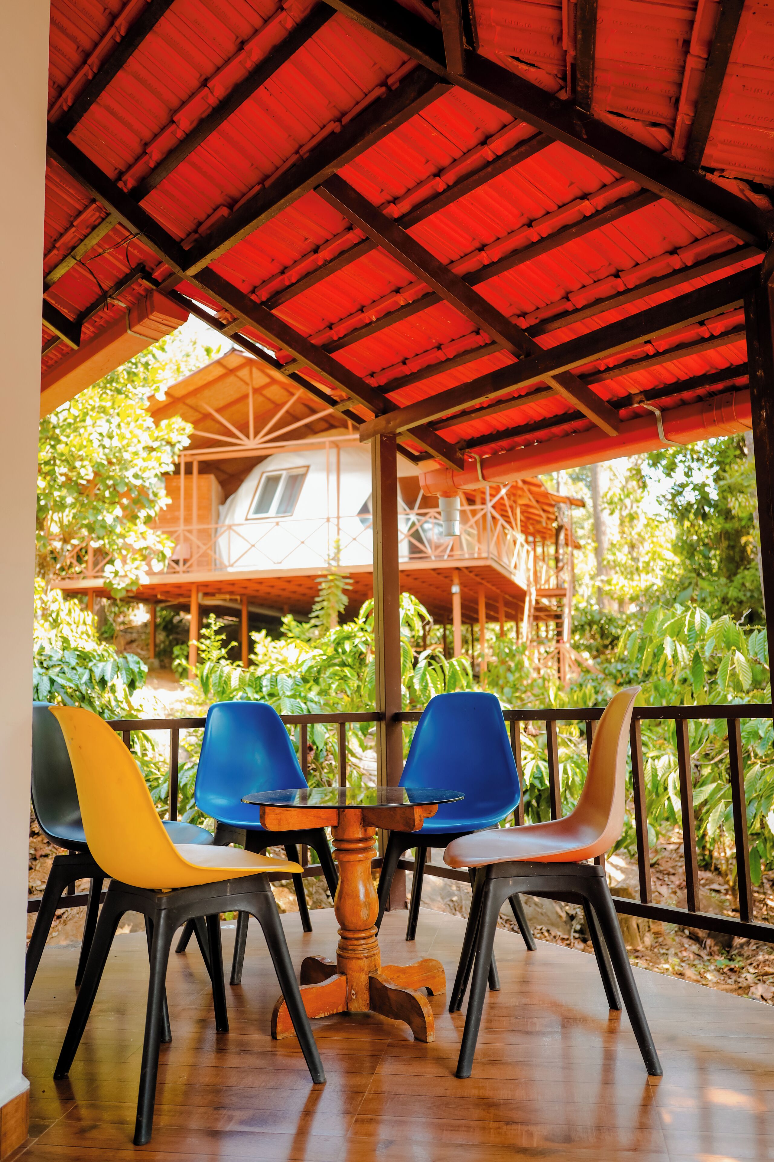 A covered outdoor seating area with a table and chairs, overlooking a wooden structure with a balcony.