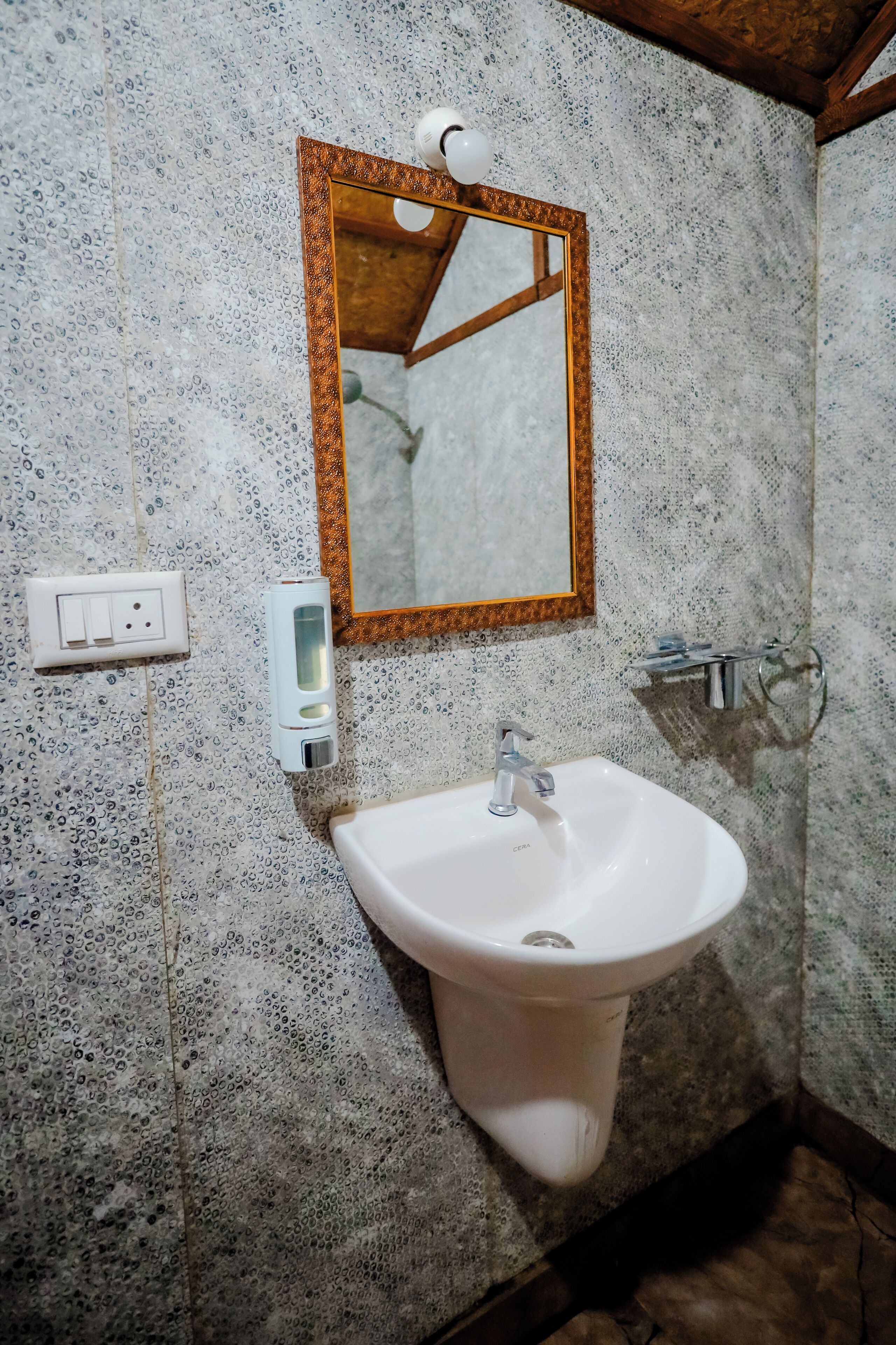 A bathroom with a white sink, a mirror with a wooden frame, a soap dispenser, and a towel rack.