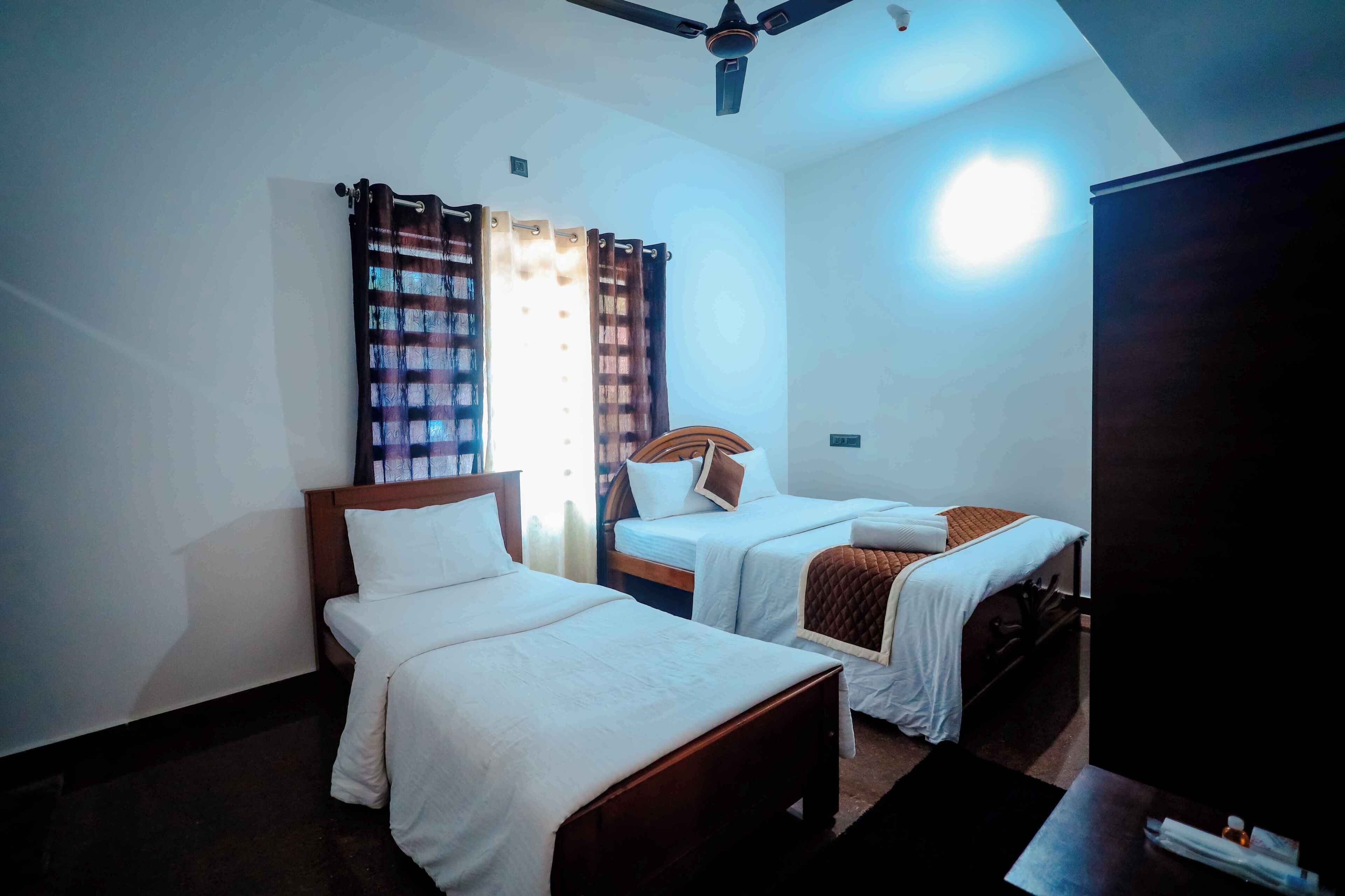 A hotel room with two single beds, a ceiling fan, and a large wardrobe.