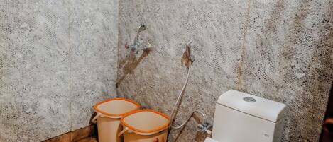 A small, rustic bathroom with a wooden ceiling, a white toilet, and two beige buckets.