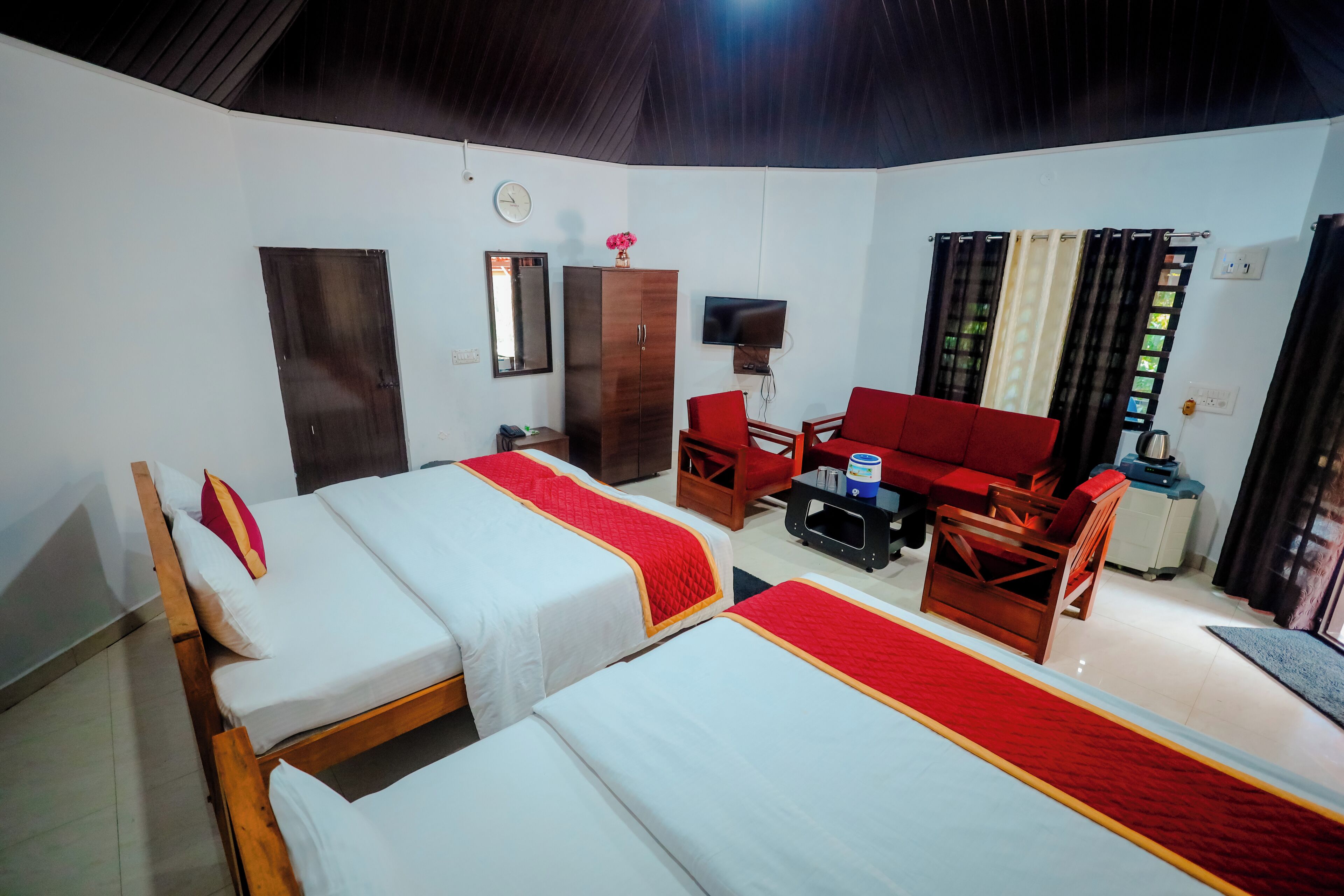 A hotel room with two single beds, a red sofa, a wooden chair, a small table, a TV, and a wardrobe.
