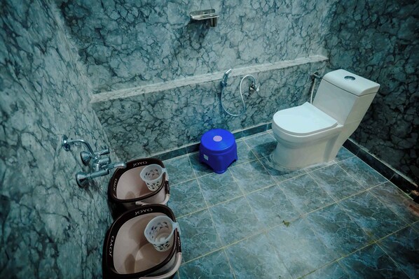 A bathroom with a marble wall, a white toilet, and two black sinks with white faucets.
