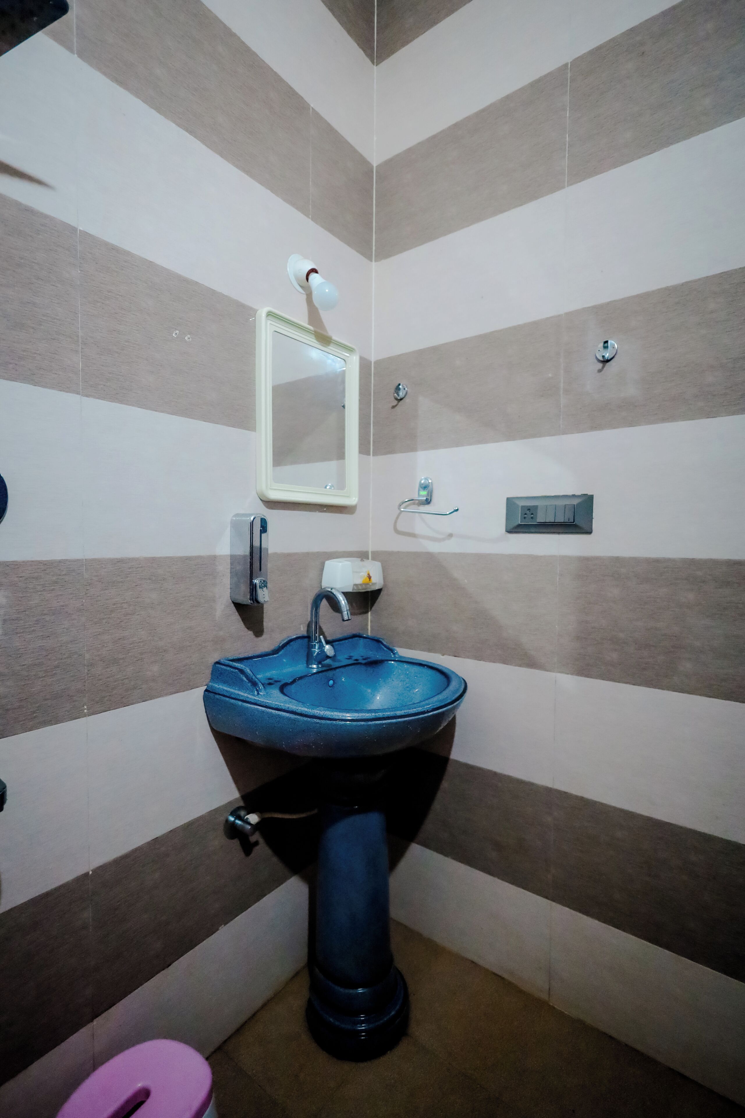 A bathroom with striped walls, a blue sink, a mirror, and a toilet.