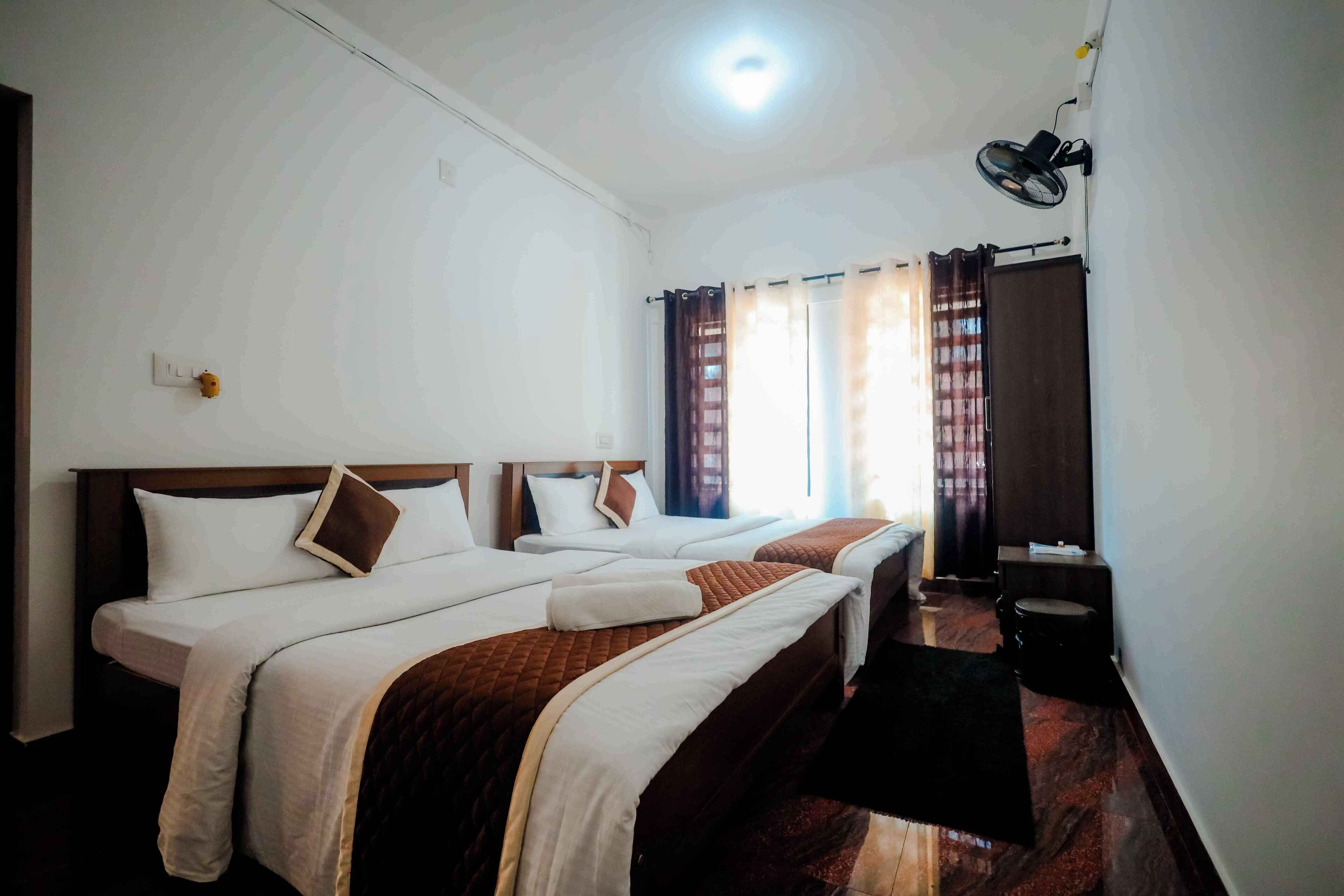 Une chambre d’hôtel avec deux lits, un ventilateur de plafond et une fenêtre avec des rideaux.
