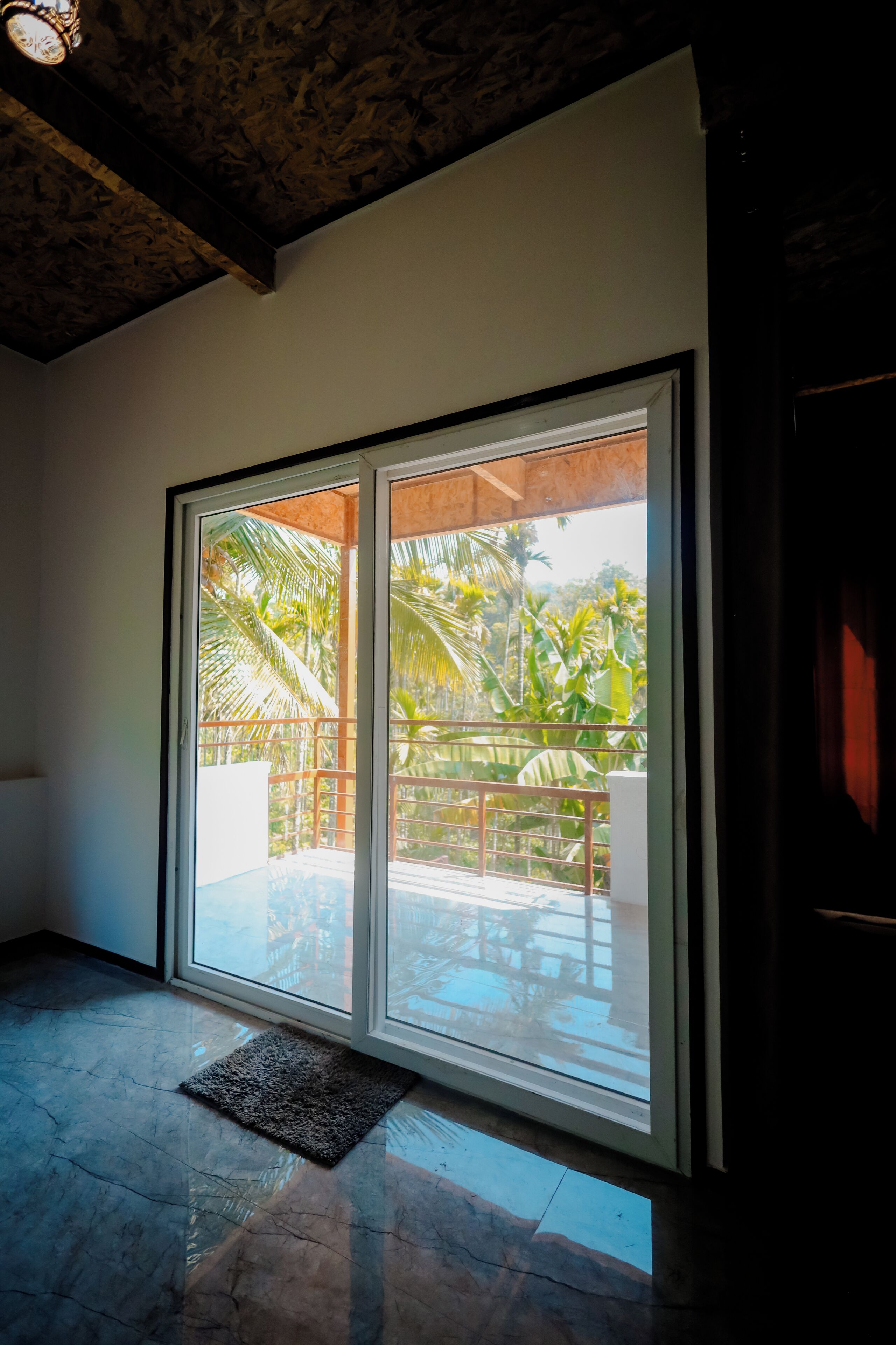 A room with a large sliding glass door leading to a balcony with a pool and tropical plants.