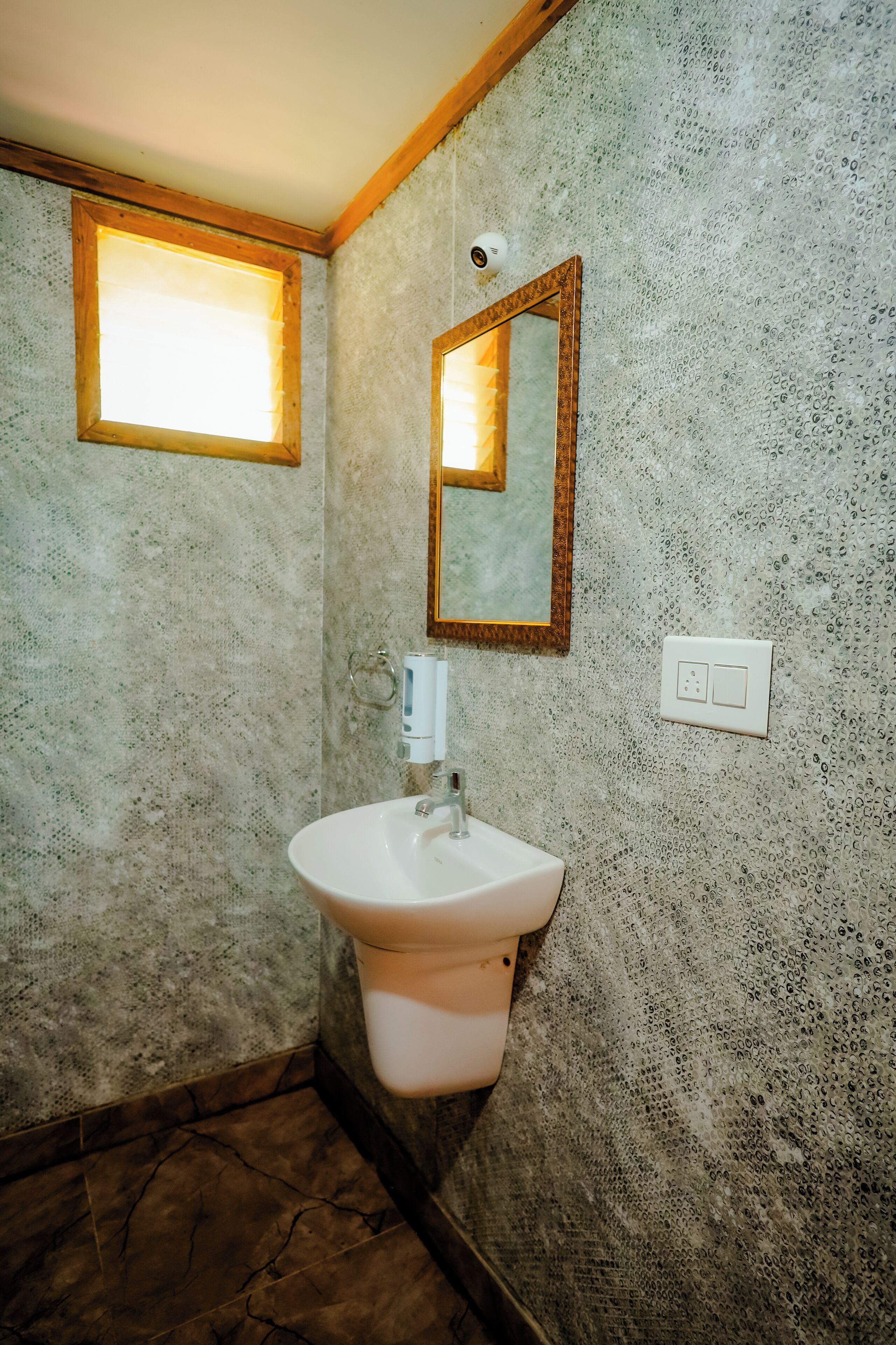 A bathroom with a textured wall, a white sink, a mirror, and a window with a wooden frame.