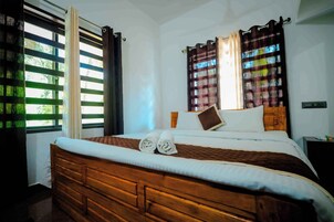 Una cama bien hecha con cabecera de madera, una ventana con persianas y una mesita de noche con lámpara.