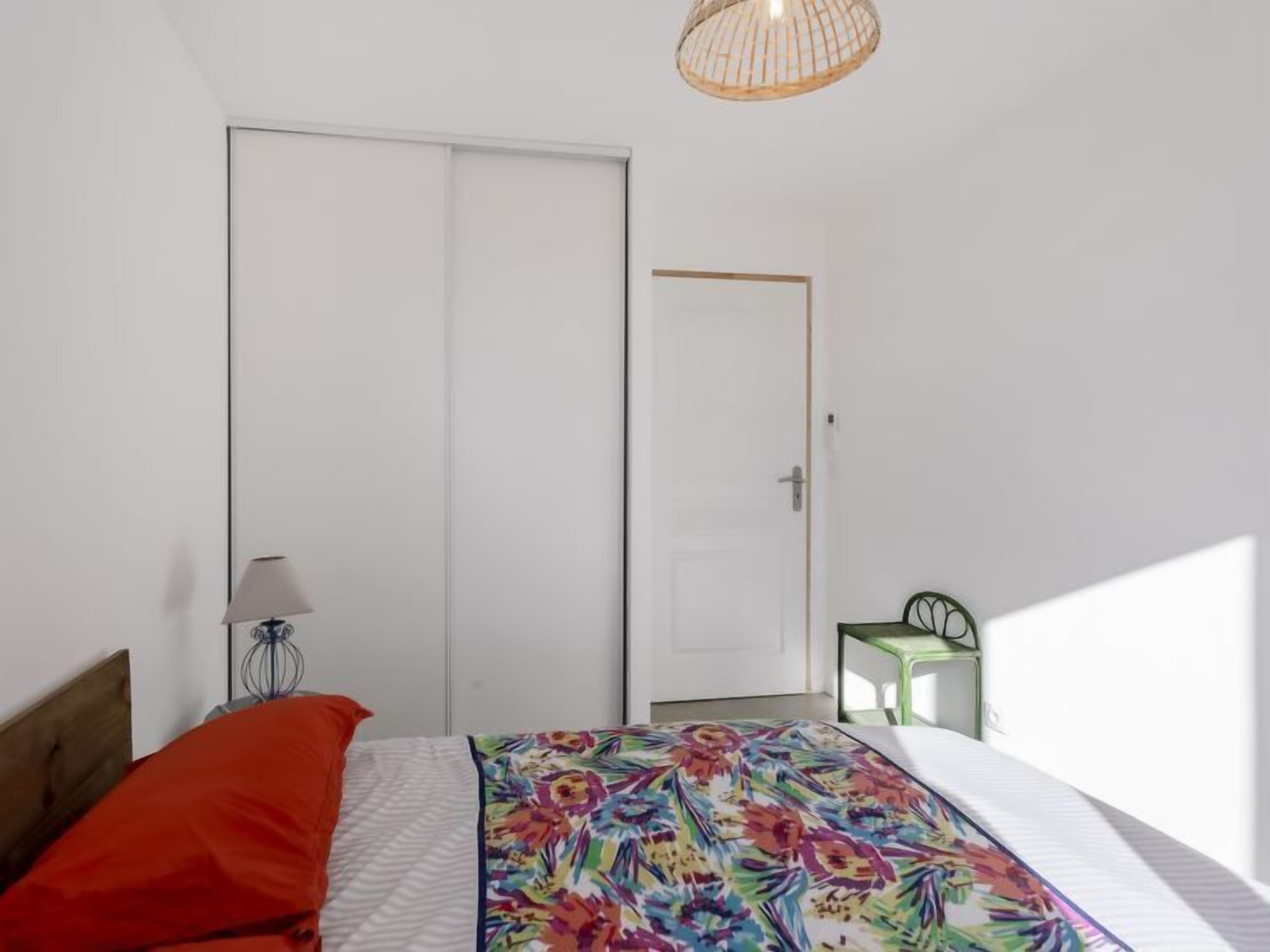 Un dormitorio con cama, mesita de noche, silla y puerta.