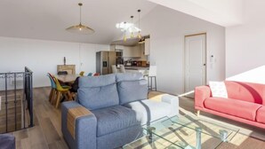A modern living room with a grey sofa, a red sofa, and a glass coffee table. There is a dining area with a wooden table and colorful chairs. The kitchen is visible in the background with white cabinets and a stainless steel refrigerator. - Gazanias by Interhome (Bormes-les-Mimosas)
