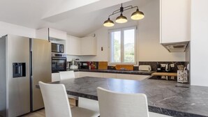 A modern kitchen with a central island, white chairs, a stainless steel refrigerator, and a window providing natural light. - Gazanias by Interhome (Bormes-les-Mimosas)
