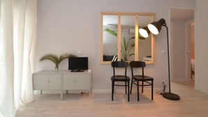 Ein modernes Wohnzimmer mit einem weißen Schrank, einem Fernseher, zwei Sesseln, einer Stehlampe und einem großen Spiegel.