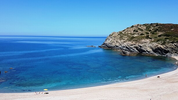 A beach with clear blue water, sandy shore, and rocky cliffs.