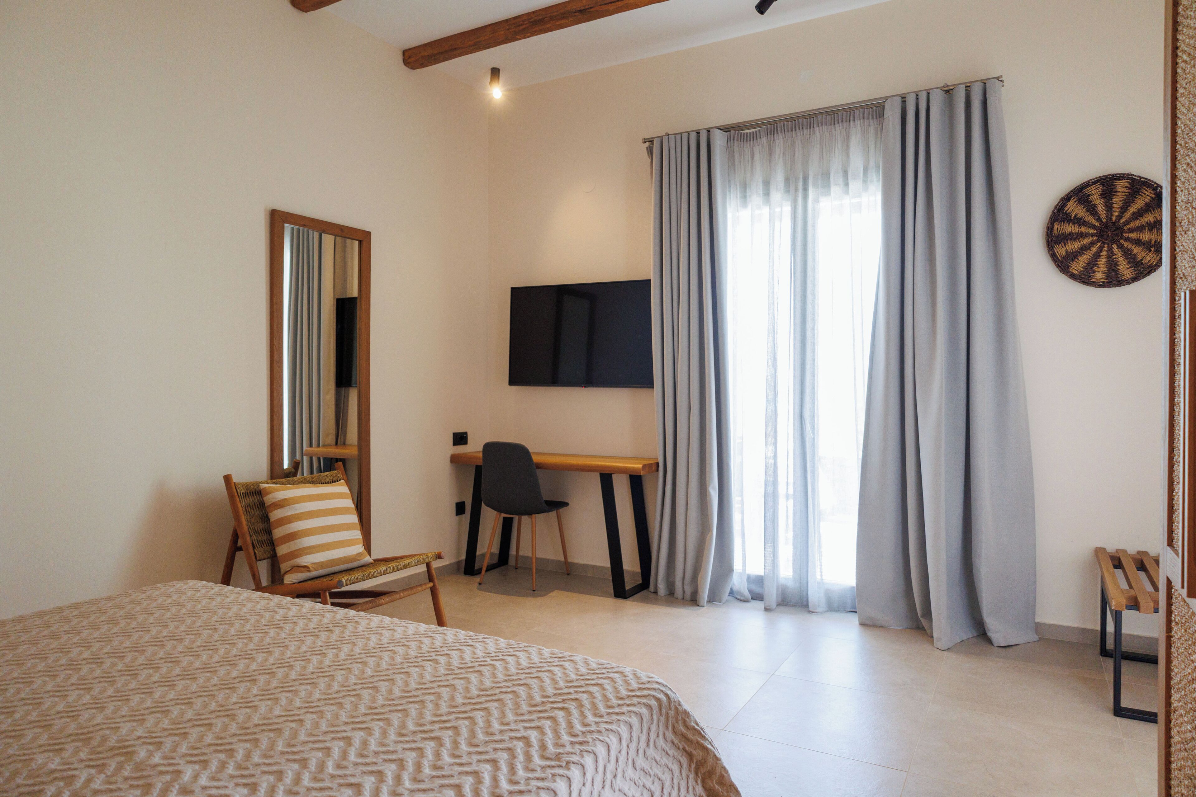 A bedroom with a bed, a desk with a chair, a television, and a window with curtains.