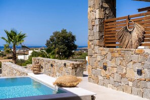 A stone pool with a view of the sea, a wooden bench, and a woven basket.