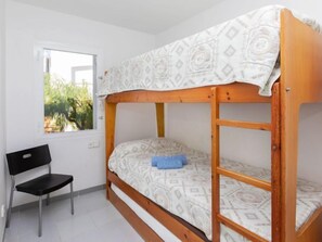 A bunk bed with a patterned bedspread, a black chair, and a window with a view of greenery.