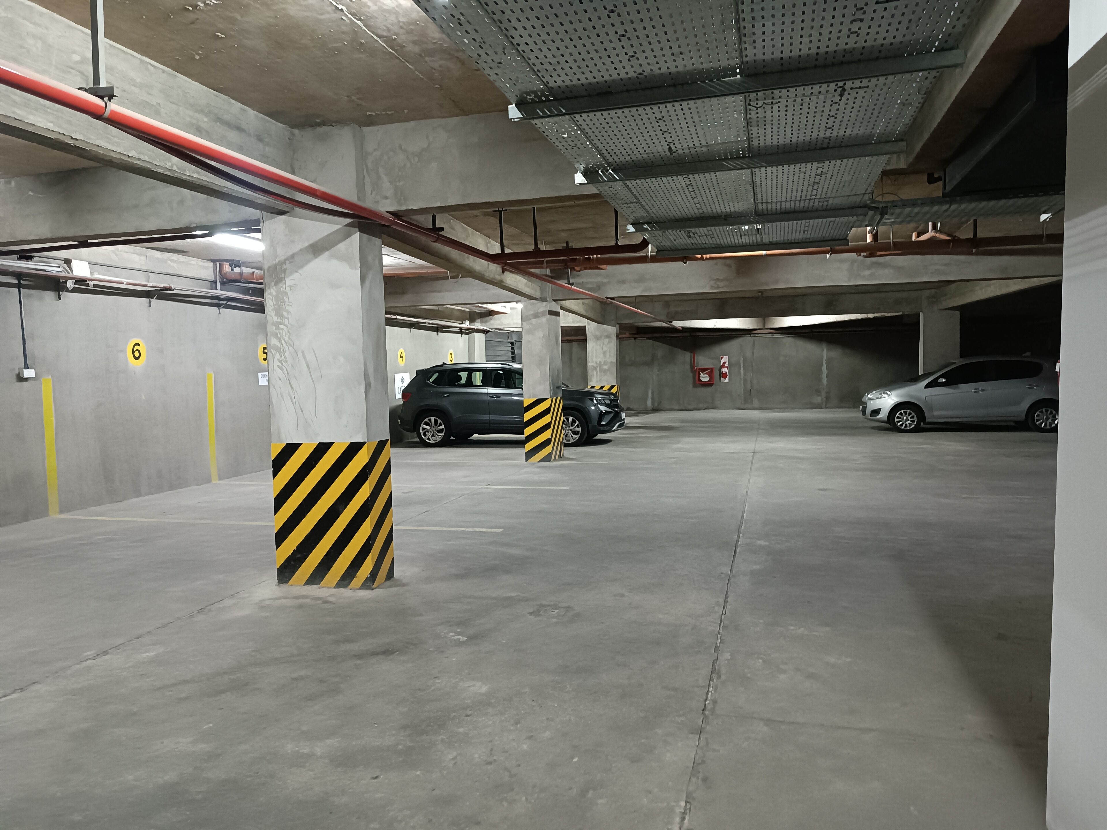 A multi-level underground parking garage with concrete pillars, marked parking spaces, and visible fire safety equipment.