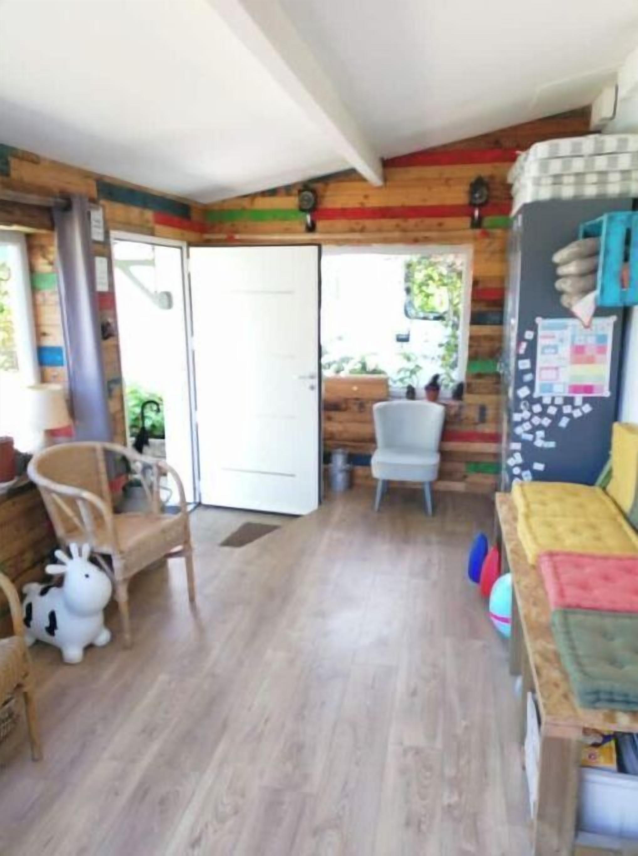 Una habitación acogedora con suelo de madera, una puerta blanca, una mesita con una silla y una pared colorida con un tablón de anuncios.