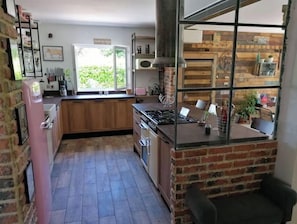 A kitchen with a brick wall, a large window, and a dining area with a table and chairs.