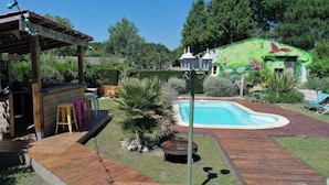 Ein Garten mit Pool, Holzterrasse und überdachtem Sitzbereich.