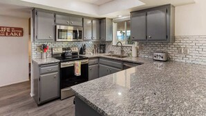 A modern kitchen with granite countertops, stainless steel appliances, and grey cabinetry. - Desert Home w/ Pool & Spa + Games (Lake Havasu City)