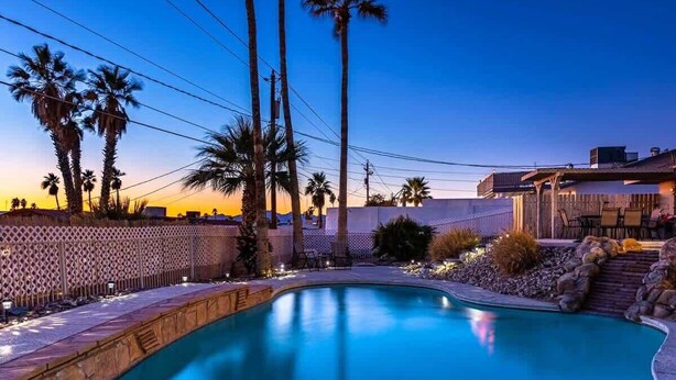 A swimming pool with a wooden deck, palm trees, and a fence. - Desert Home w/ Pool & Spa + Games (Lake Havasu City)