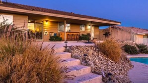 A two-story house with a covered porch, outdoor seating, and a swimming pool. - Desert Home w/ Pool & Spa + Games (Lake Havasu City)