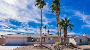 A single-story house with a garage, surrounded by palm trees and a clear sky. - Desert Home w/ Pool & Spa + Games (Lake Havasu City)
