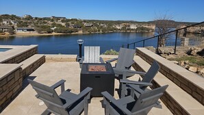 An outdoor patio with a fire pit and seating area overlooking a lake, surrounded by stone walls and a clear view of the lake and distant buildings. - *New PK SLIDE* 5 bed, 6 bath home with pool/hot tub. Hell's Gate View!! (Strawn)