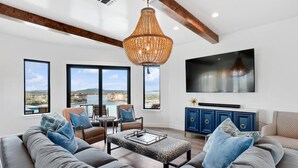 A modern living room with a large chandelier, a flat-screen TV, and a view of the outdoors. - *New PK SLIDE* 5 bed, 6 bath home with pool/hot tub. Hell's Gate View!! (Strawn)