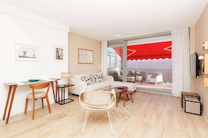 Uma sala de estar moderna com um sofá branco, uma mesa de jantar com cadeiras, uma cadeira de vime, uma televisão e uma varanda com toldo vermelho.
