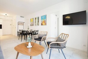 Un soggiorno moderno con un tavolo rotondo in legno, sedie in vimini, un televisore a schermo piatto e una zona pranzo con sedie nere.