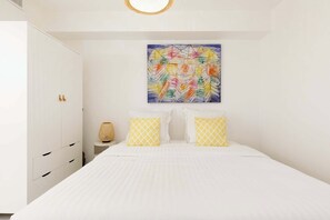 Una camera da letto con un letto, pareti bianche, un quadro e un comodino.