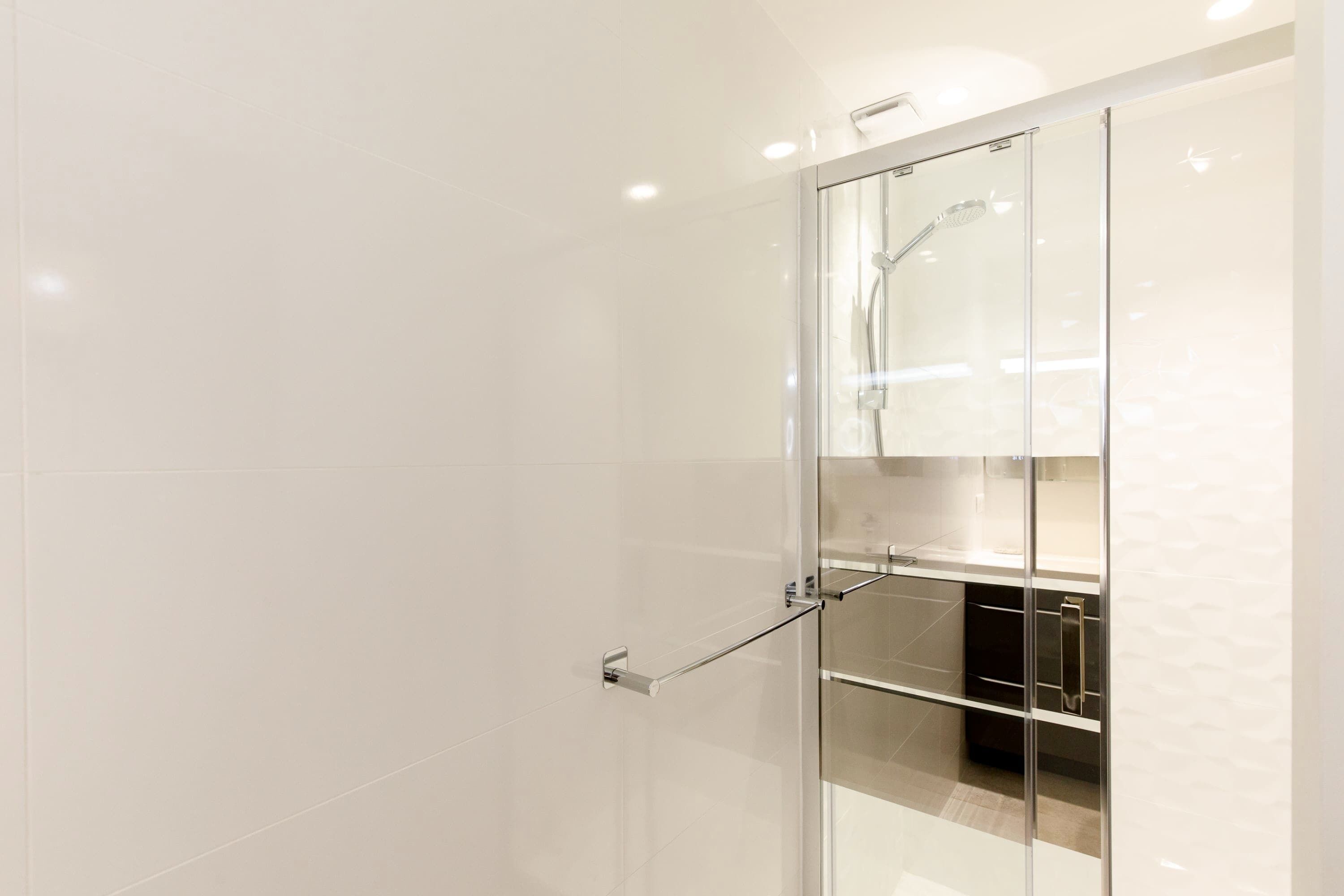 Ein modernes Badezimmer mit Duschkabine aus Glas, Handtuchhalter und sichtbarem Stauraum.