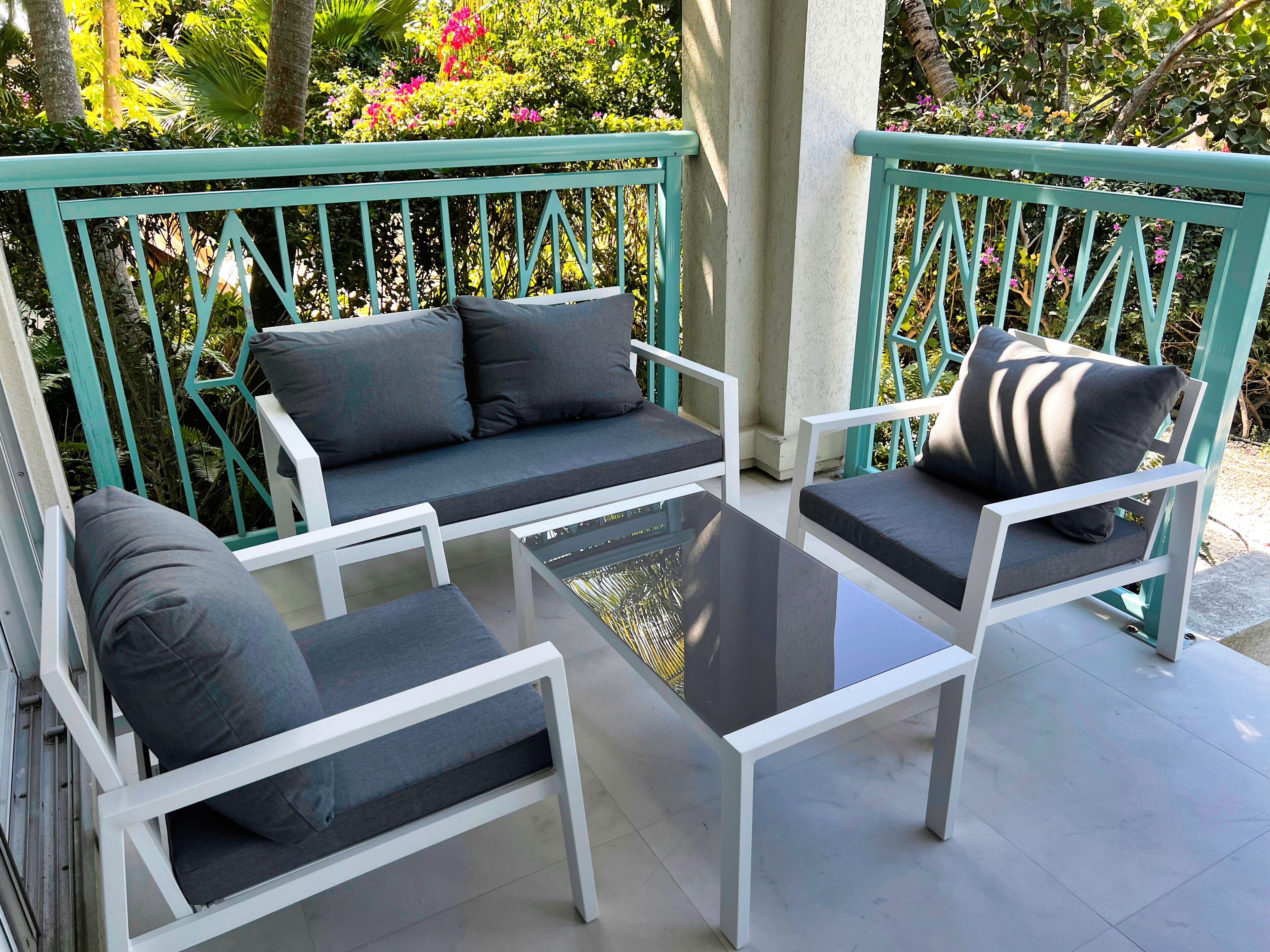 Eine Terrasse mit einer weißen Couch, zwei weißen Stühlen und einem Glastisch.