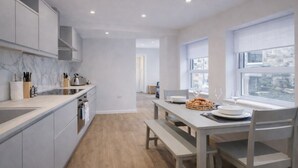 Una cucina moderna con mobili bianchi, un piano di lavoro in marmo e un'area pranzo con tavolo e sedie.